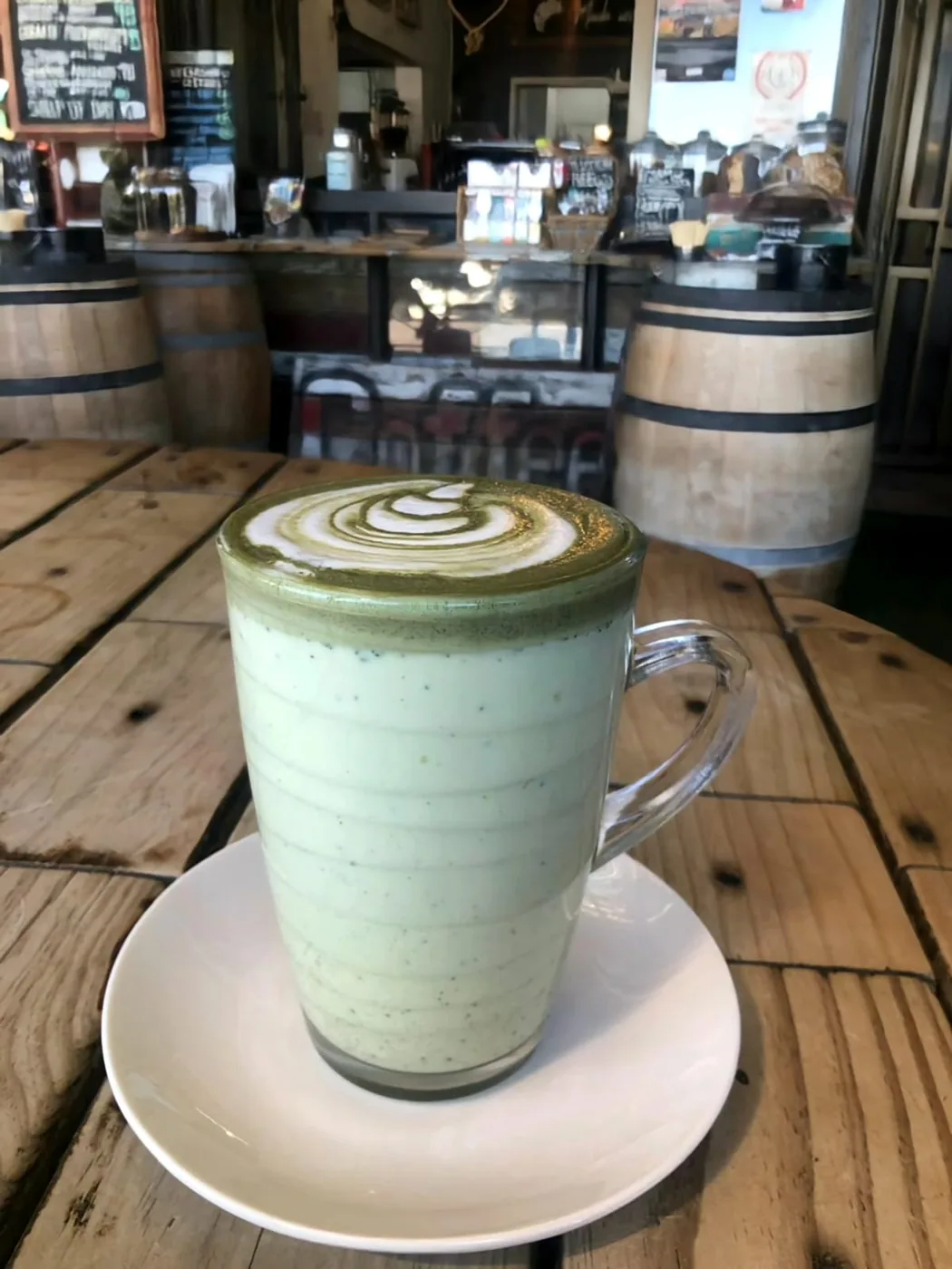 A matcha latte with latte art by the wine barrels.